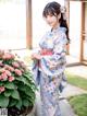 A woman in a blue kimono standing next to a flower pot.