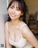 A woman in a white tank top leaning against a wall.