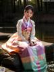 A woman in a colorful dress sitting on a rock by the water.