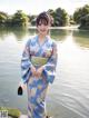 A woman in a blue kimono standing by a lake.