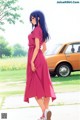 A woman in a pink dress standing in front of a car.